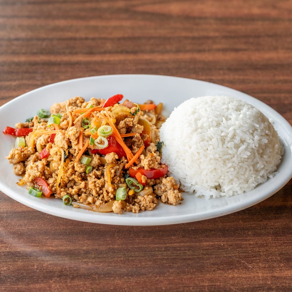 A white plate with a serving of Thai basil chicken (Pad Krapow Gai) and white rice.