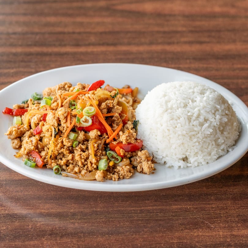 A white plate with a serving of Thai basil chicken (Pad Krapow Gai) and white rice.