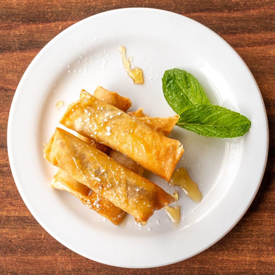 Golden fried spring rolls drizzled with honey and powdered sugar, garnished with fresh mint.
