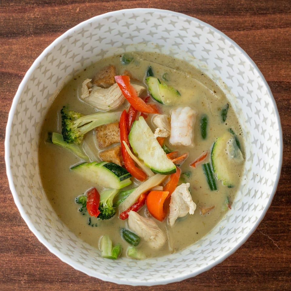 A white bowl with a star pattern filled with green curry, chicken, shrimp, and vegetables.