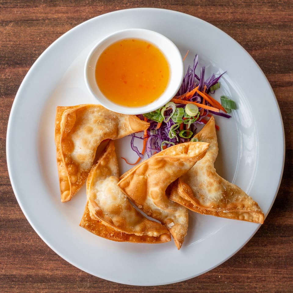 Crispy fried wontons with a side of sweet chili dipping sauce and shredded vegetables.