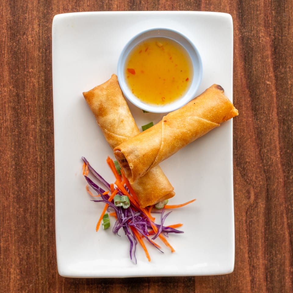 Two crispy spring rolls with sweet chili sauce and shredded cabbage on a white plate.